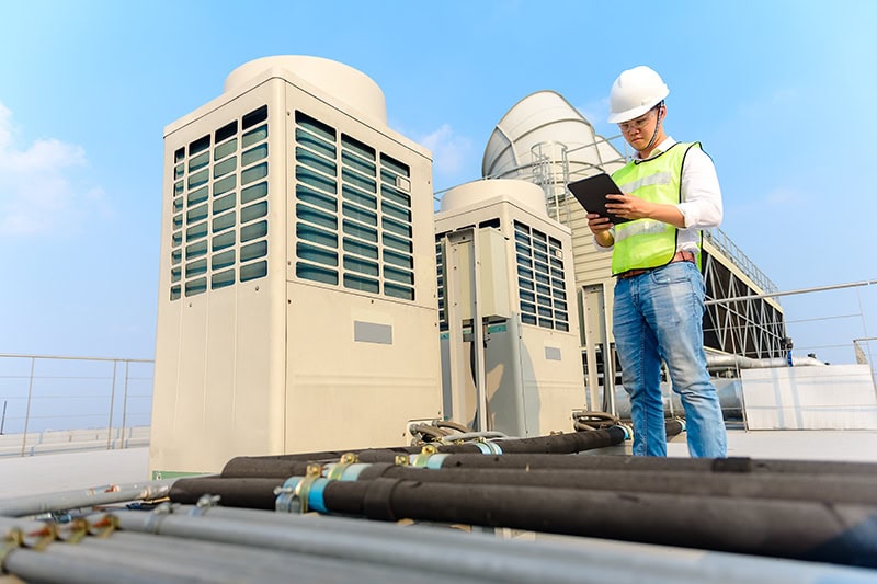 Commercial HVAC technician holding maintenance checklist and looking at HVAC system at a local business.